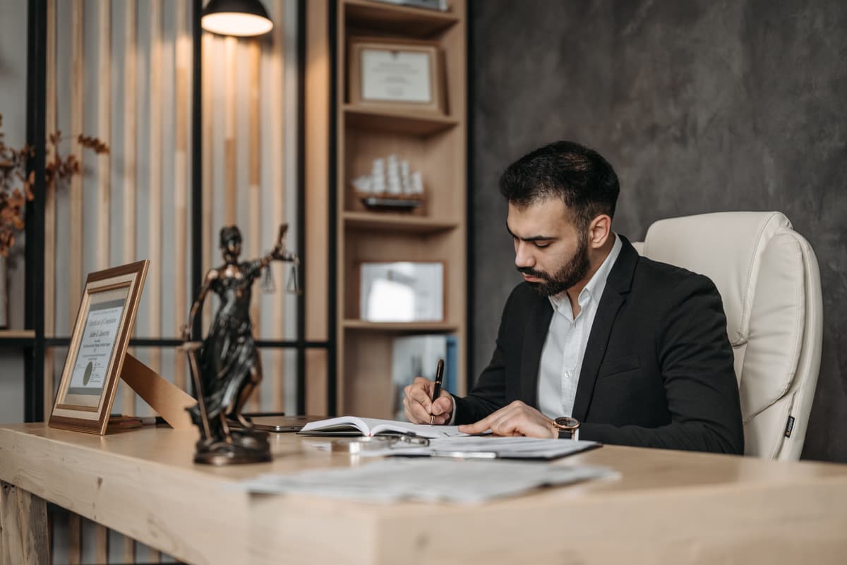 Professional portrait of a male lawyer leaning against a desk in a library setting
